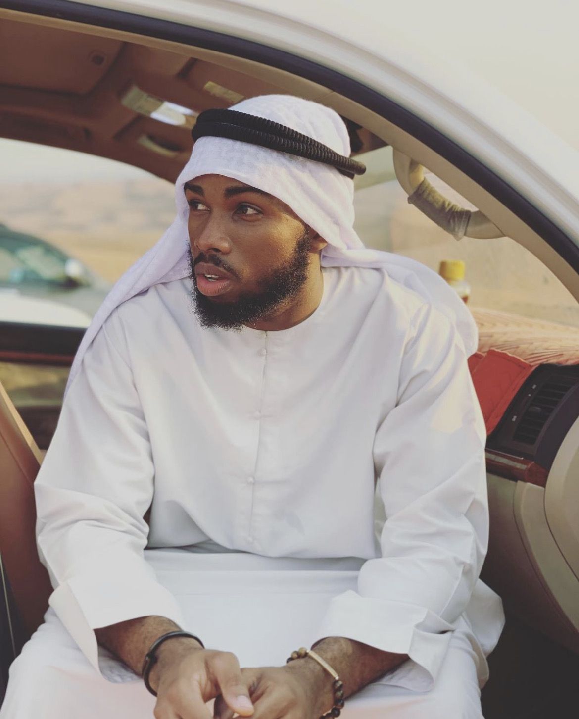 OJ in a kandura and headscarf sitting in a car