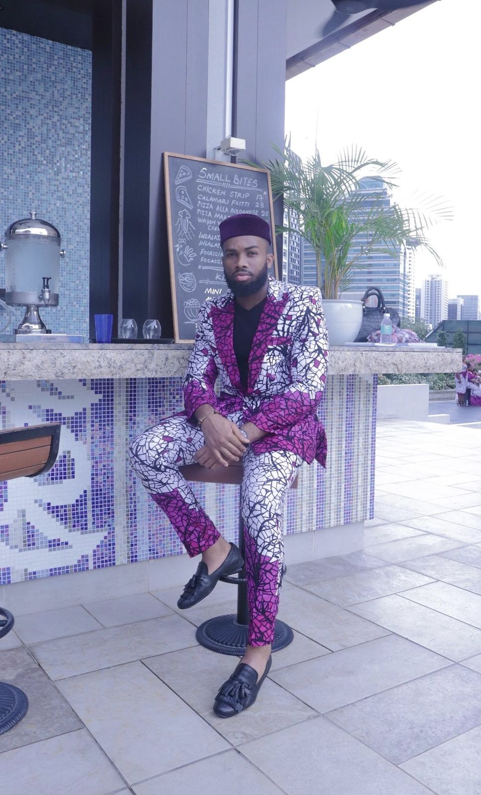 OJ in a patterned suit on a stool at a rooftop bar