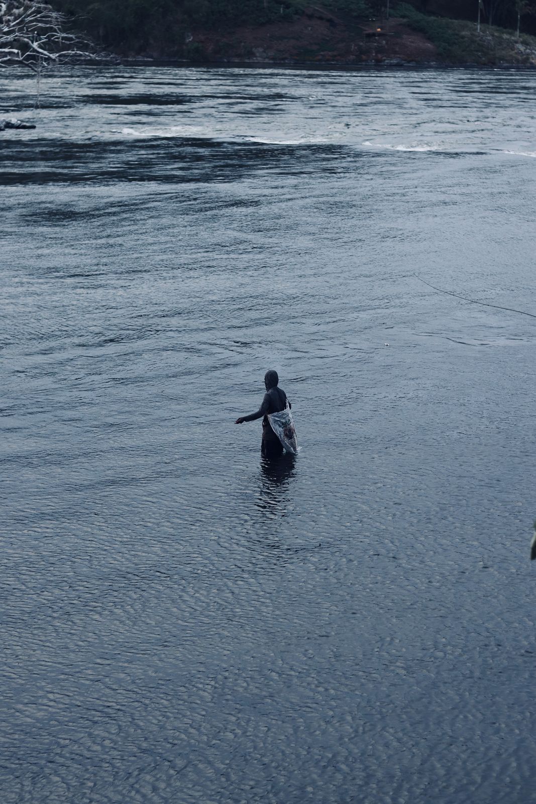 A man standing waist-deep in a wide river