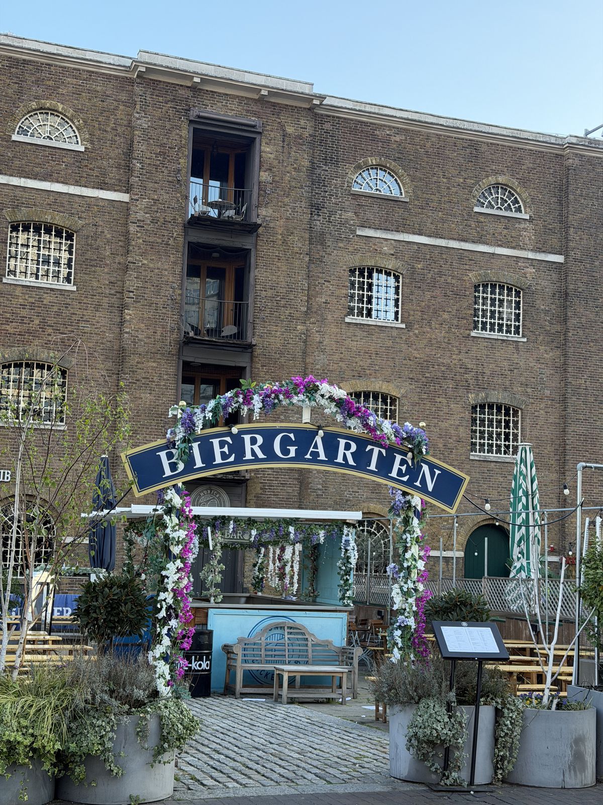 A flower-covered Biergarten sign in front of a brick warehouse